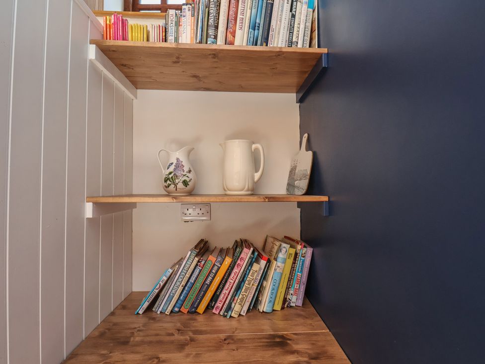 A bookshelf with books and jugs in a library at Fleming Cottage