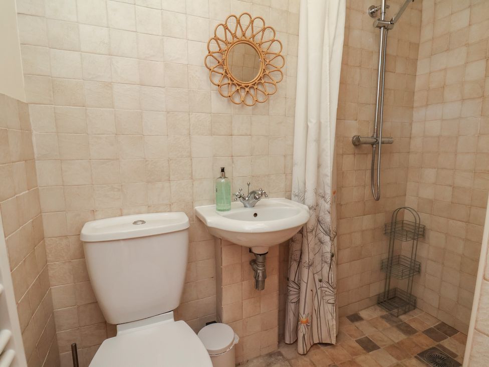 A bathroom with a shower, toilet, mirror, and sink at Fleming Cottage