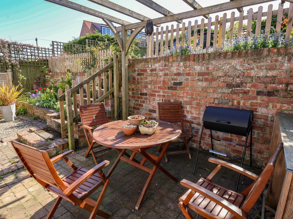 A garden with a wooden table and chairs near a grill at Fleming Cottage