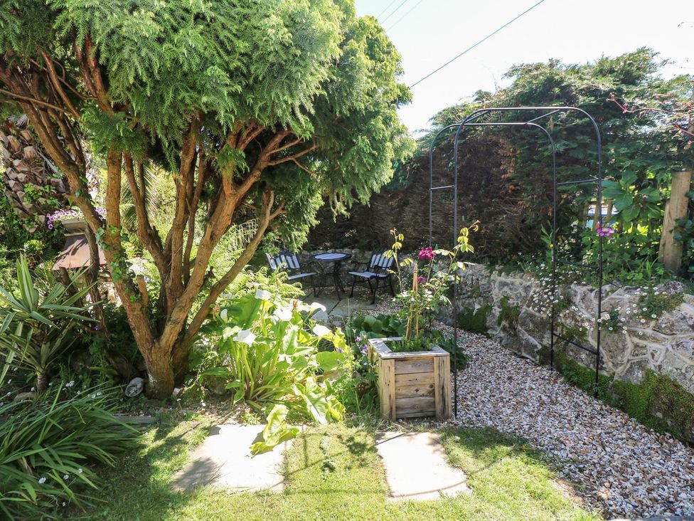 A garden with a tree, table, chairs and flowers at Tinners Way in Helston