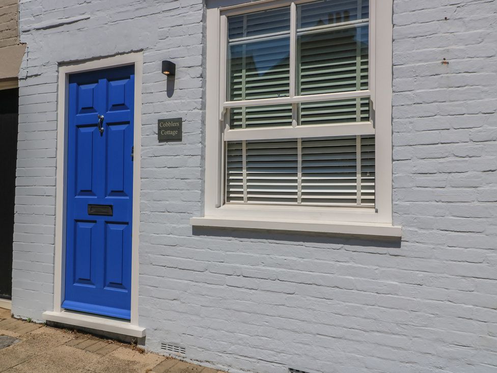 A blue door and window on a brick wall at Cobblers Cottage in Lymington
