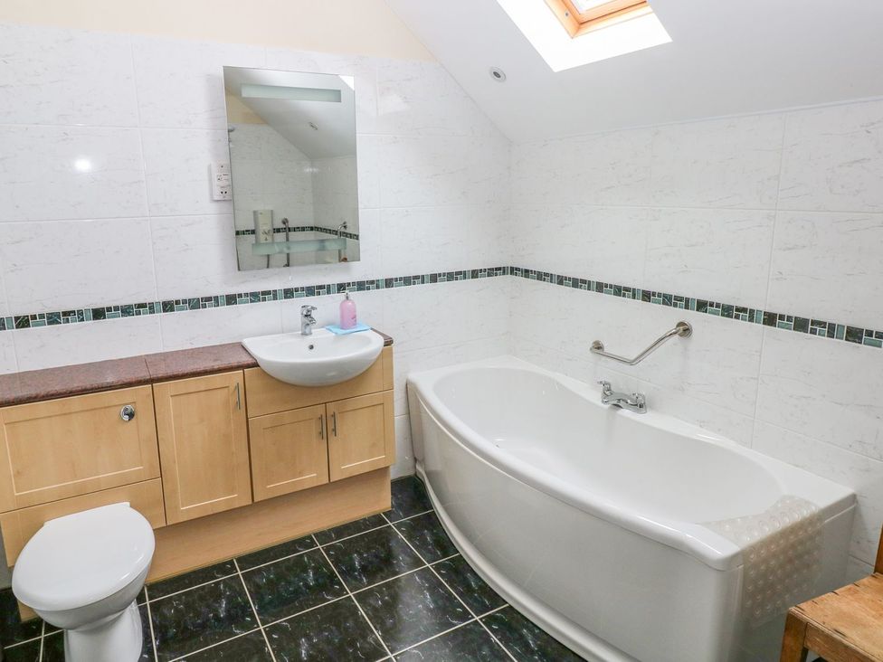 A bathroom with a bath tub, toilet, sink and cabinet at Maerdy Cwtch in Haverfordwest
