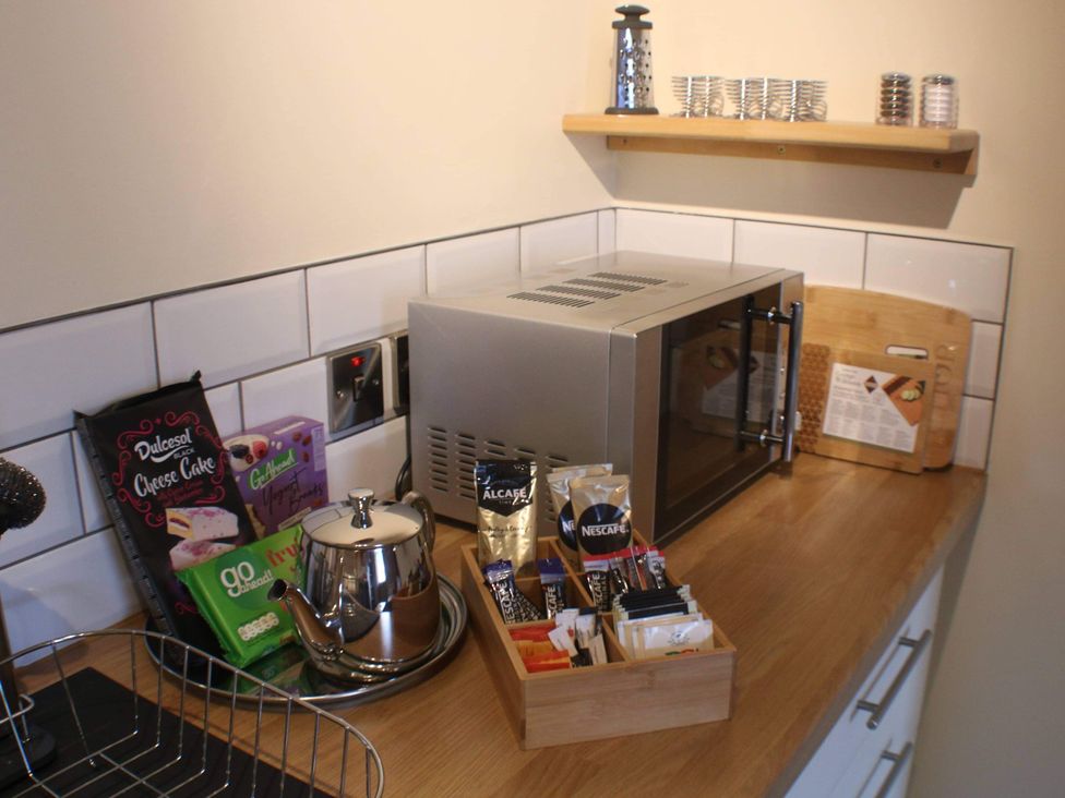 A kitchen counter with a microwave, teapot, and assorted tea and cake items at Stylish Highland retreat in the heart of town, Pitlochry
