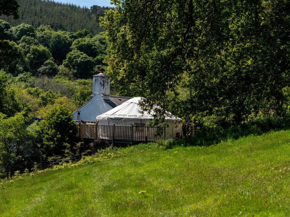 A yurt with a deck and chimney surrounded by trees at Hapus Yurt - Two Beautiful Yurts and Barn Cottage