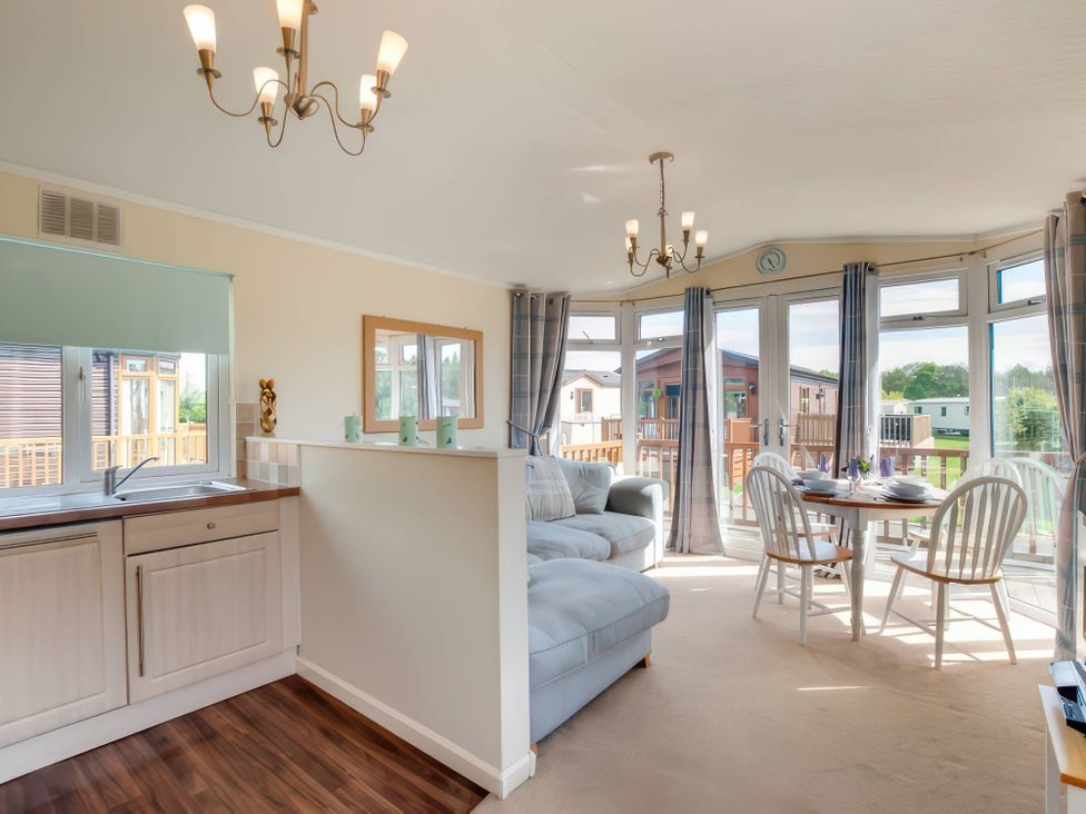 A living room with a kitchen area and a table with chairs at Pet-friendly lodge with hot tub near the coast