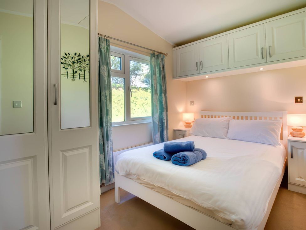 A bedroom with a bed, wardrobe, and window at Pet-friendly lodge with hot tub near the coast