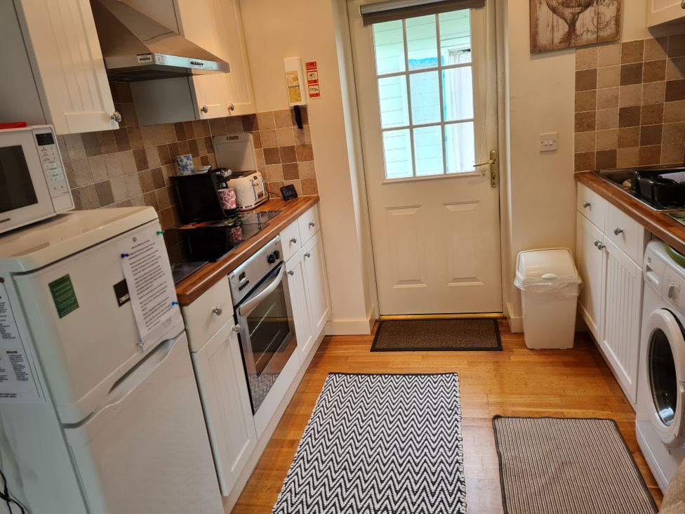 A kitchen with appliances and a door at Riverside cottage with otters near Tintagel