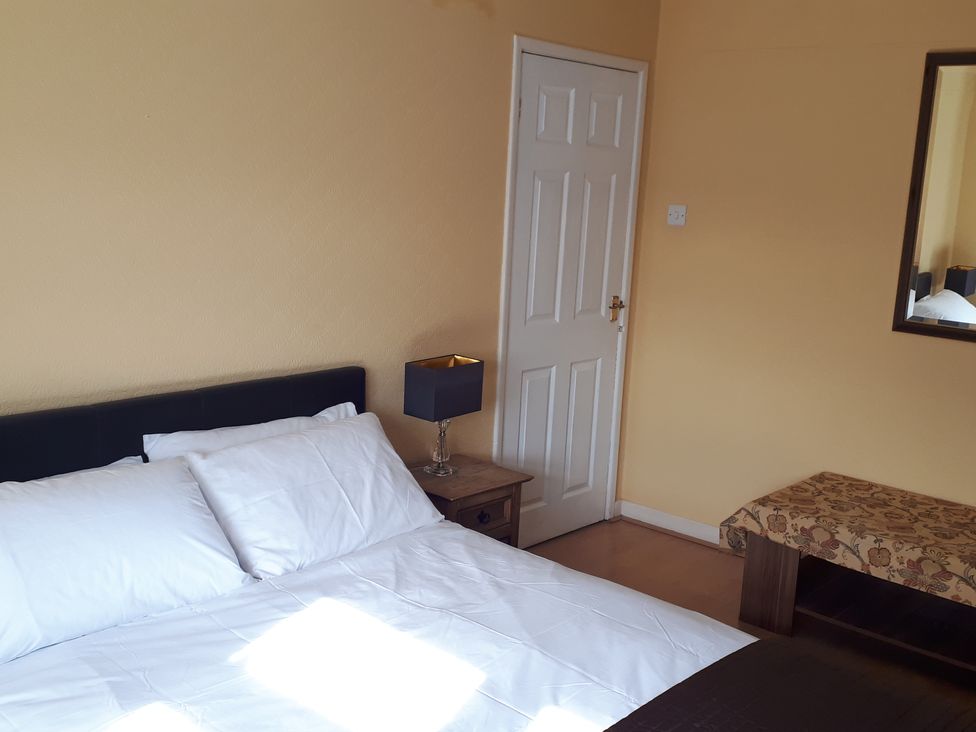 A bedroom with a bed, table, lamp, mirror, and door at tbc