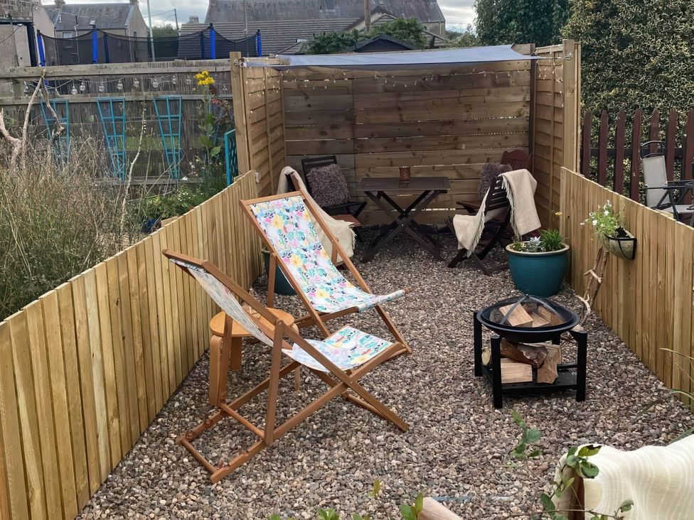 A garden with deck chairs, a wooden table, and a fire pit at Pet-friendly coastal flat with fire pit and views, Newburgh, Fife