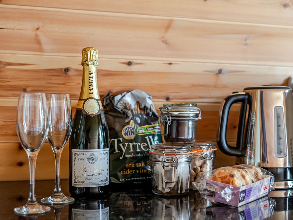 A kitchen countertop with champagne, glasses, crisps, a kettle, and pastry at Peaceful pod with bay views, walk to 3 beaches, St Ives
