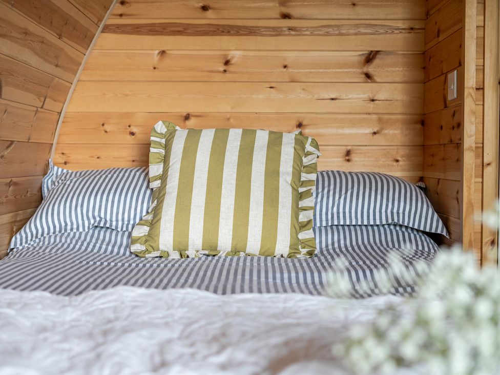 A bed with striped bedding and a decorative pillow at Peaceful pod with bay views, walk to 3 beaches in St Ives