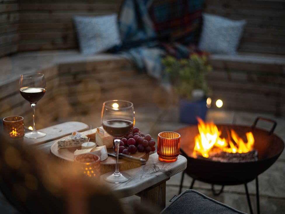 An outdoor seating area with wine glasses, cheese board, and fire pit at tbc