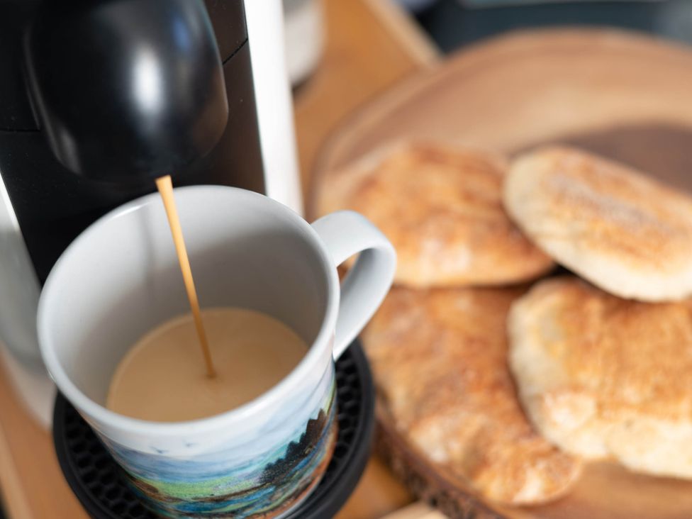A coffee machine pouring coffee into a mug near bread at tbc