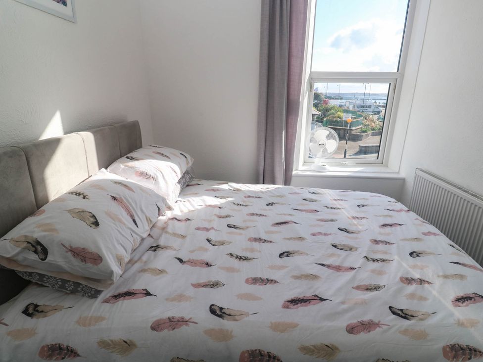 A bedroom featuring a bed with patterned sheets and a window at Flat 2 in Penzance