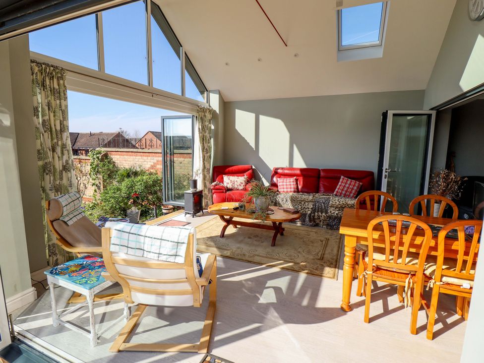 A conservatory with a red sofa and dining table at Seascape in Hunstanton