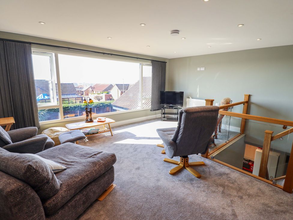 A living room with a sofa, chair, and television at Seascape in Hunstanton