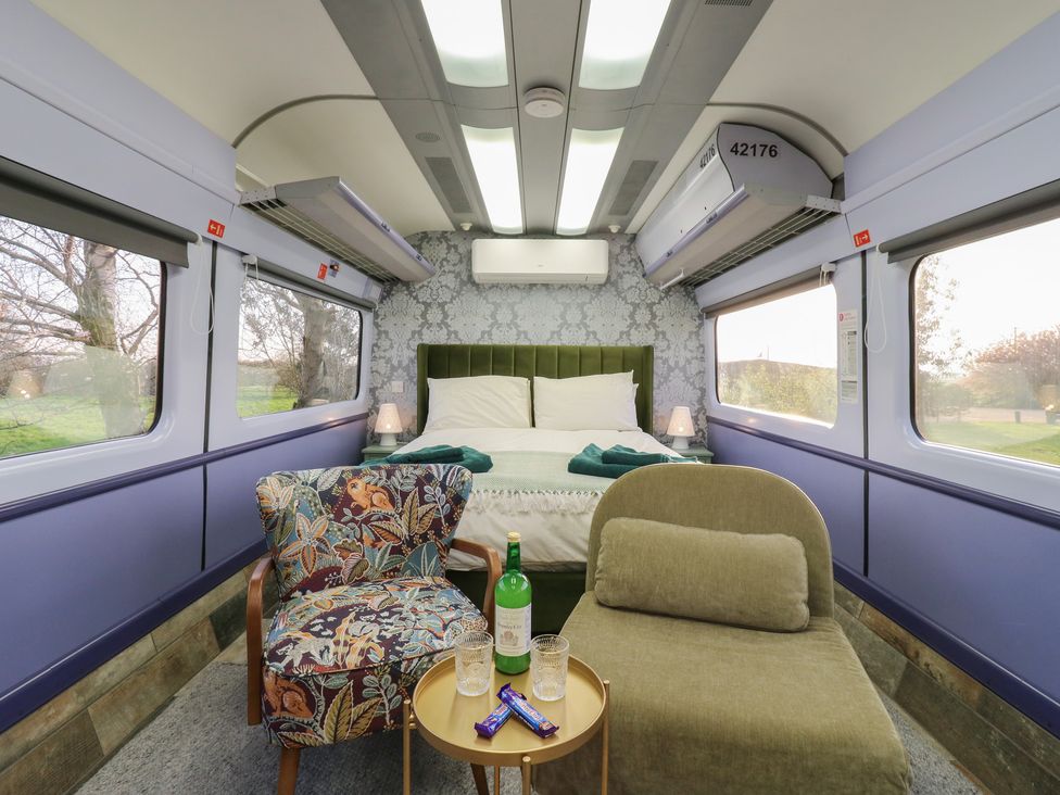 A bedroom with a bed and armchair at Penzance Railway Carriage 1 with hot tub, Ely