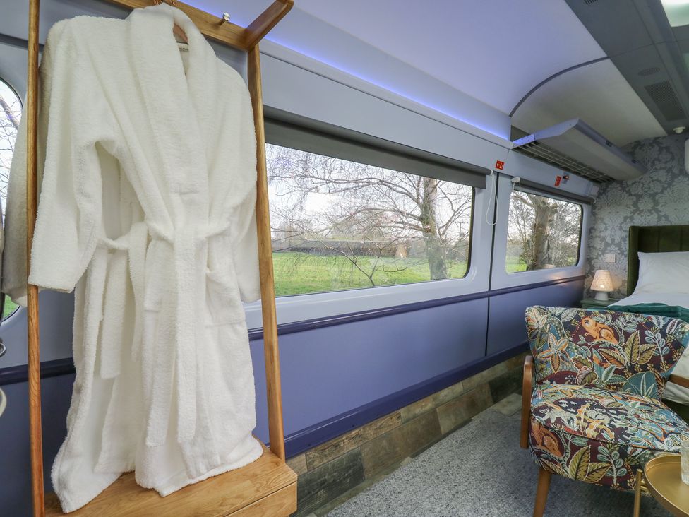 A bedroom featuring a bathrobe, a chair, and a lamp at Penzance Railway Carriage 1 with hot tub, Ely
