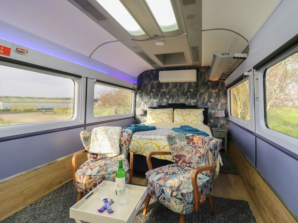 A bedroom with a bed and armchairs at Paddington Railway Carraige 2 with hot tub, Ely