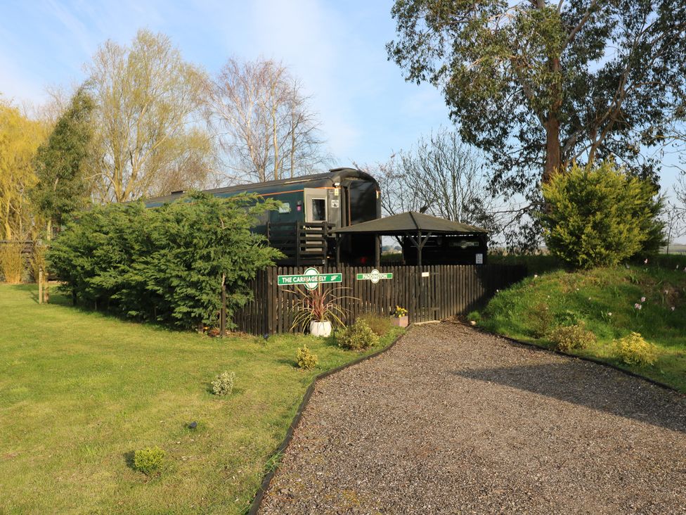 A gravel path leading to a railway carriage with a gazebo and trees at The Carnage Ely