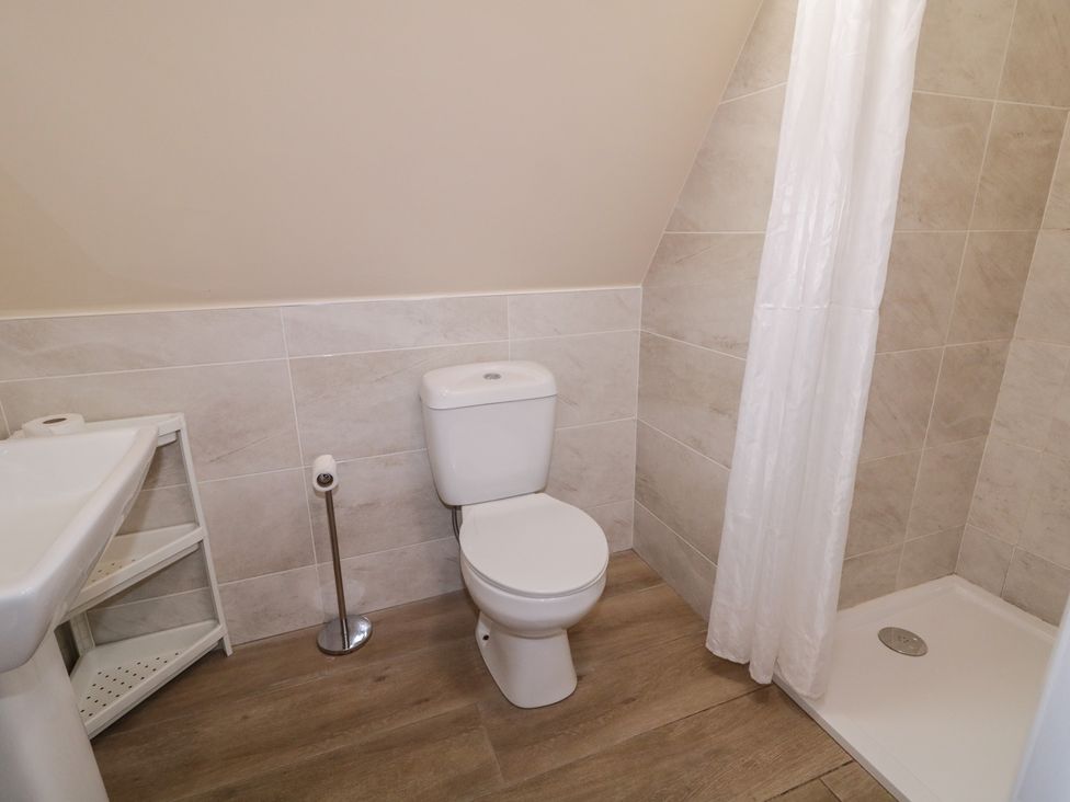 A bathroom with a toilet, sink, shower, and storage shelf at Cabin 4 Doire Chonair in Gortahawk
