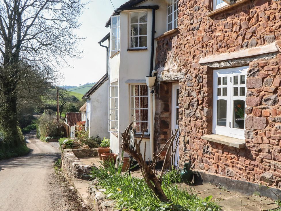 A stone building with windows and plants along a pathway at Upper Frogpool Cottage in Crediton