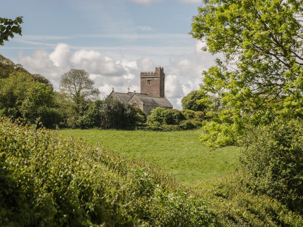 A church with a tower surrounded by trees and grass at Upper Frogpool Cottage in Crediton
