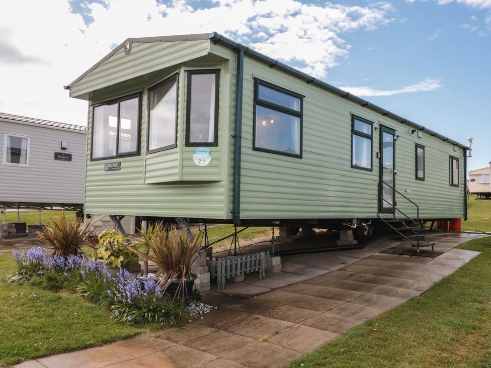A static caravan with a pathway and flower beds at 21 Dunlin Dell Flamborough