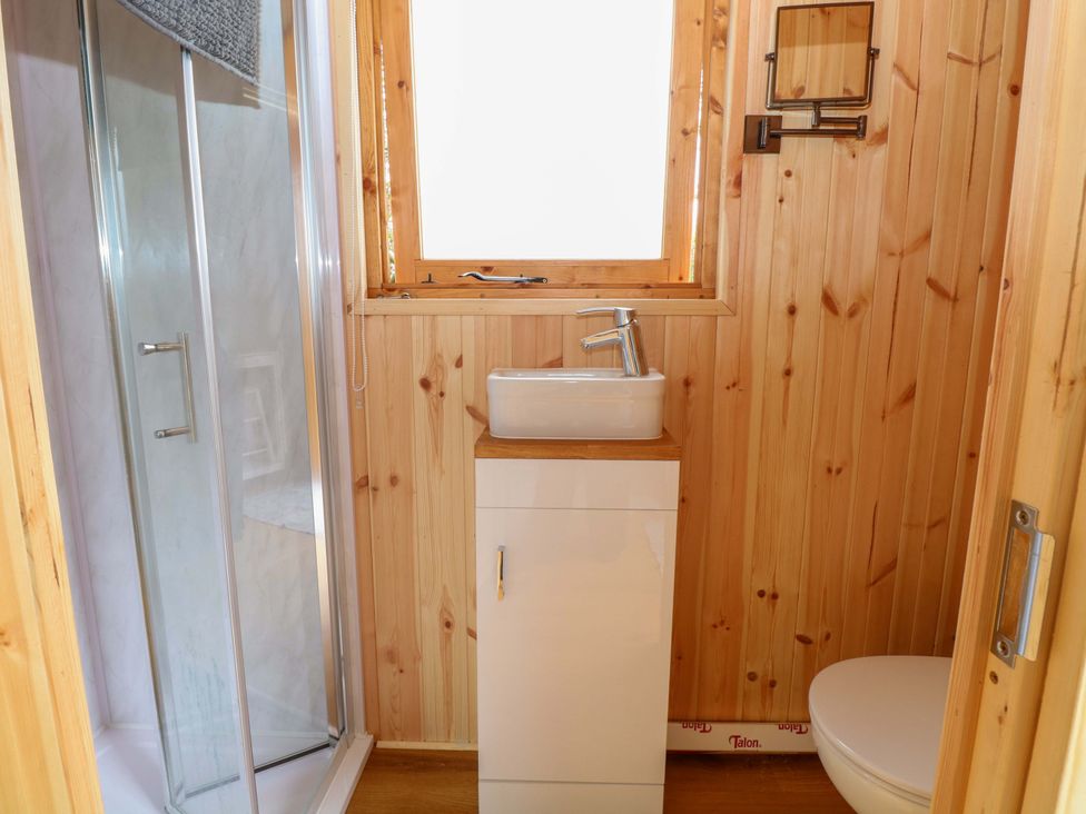 A bathroom with a shower, sink, toilet, and wooden walls at Hazel