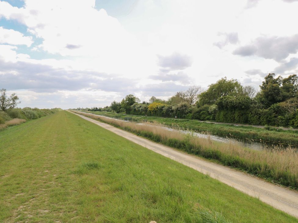 A grassy path along water with trees and a cloudy sky at Hazel