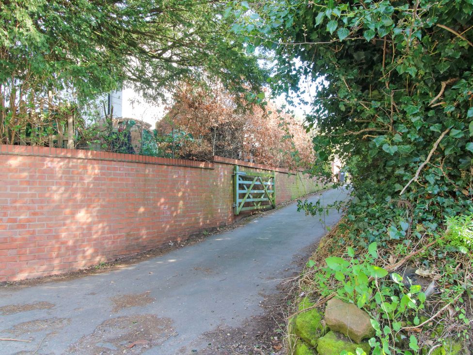 A pathway with a green gate and brick wall at Cheshire Views in Malpas