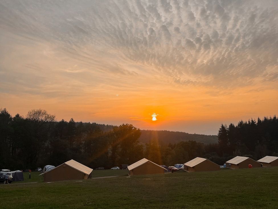 A sunset over a campground with tents and trees at Bracelands - Safari Tent 1 Coleford