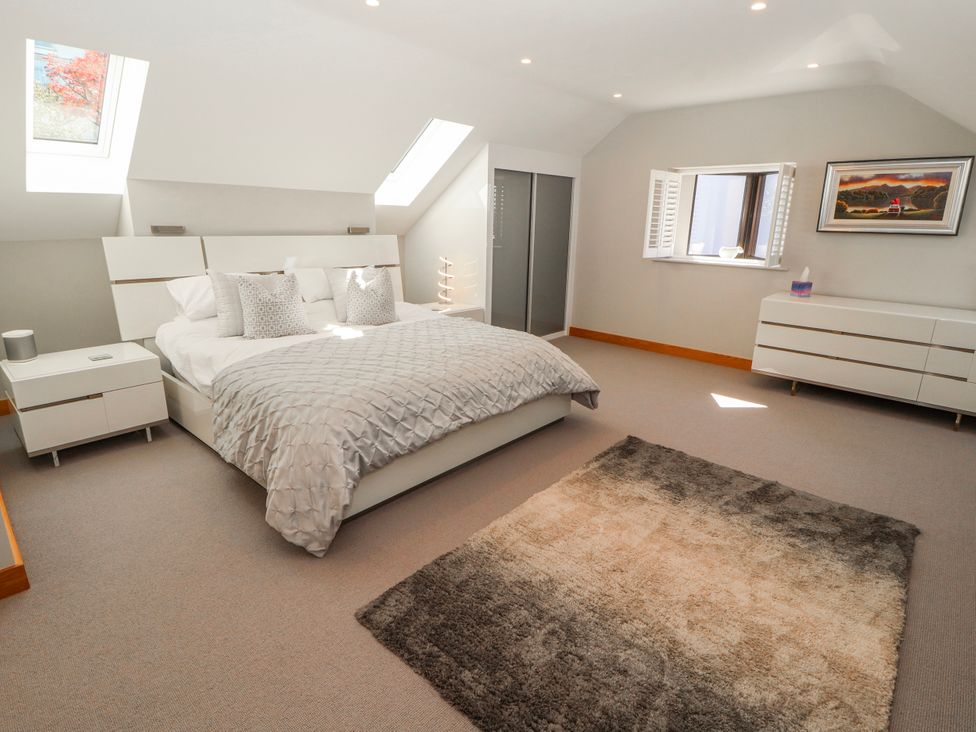 A bedroom featuring a bed, nightstand, dresser, and windows at Midways in Bowness-On-Windermere