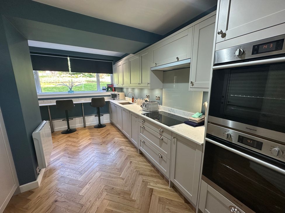 A kitchen with cabinets, stove, and bar stools at Broombank Melrose