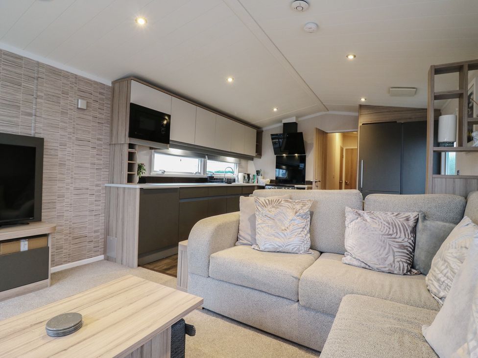A living room with a sofa and kitchen area at no 20 Barley Way in Colchester