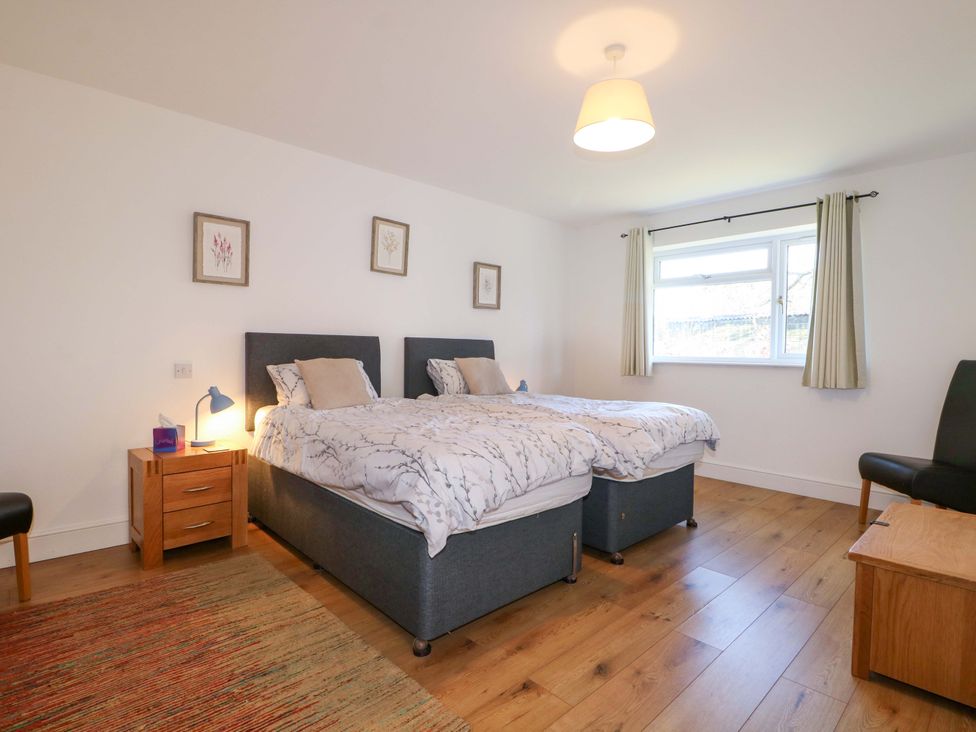 A bedroom with two beds, a nightstand, and a chair at Snowdrop Cottage in Maidstone