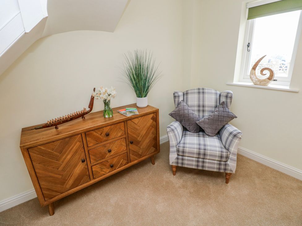 A sitting room with a chair and a cabinet at Barley Cottage in Oxwich