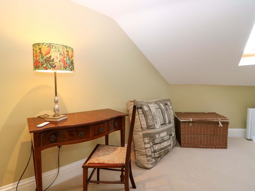 An attic with a desk, lamp, chair, cushion, and basket at Woodmarket Apartments in Kelso