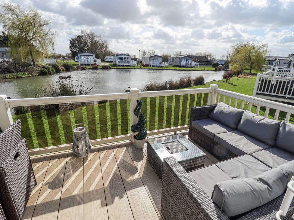 An outdoor area with a sofa and coffee table overlooking a pond at 13 The Lakes Mablethorpe