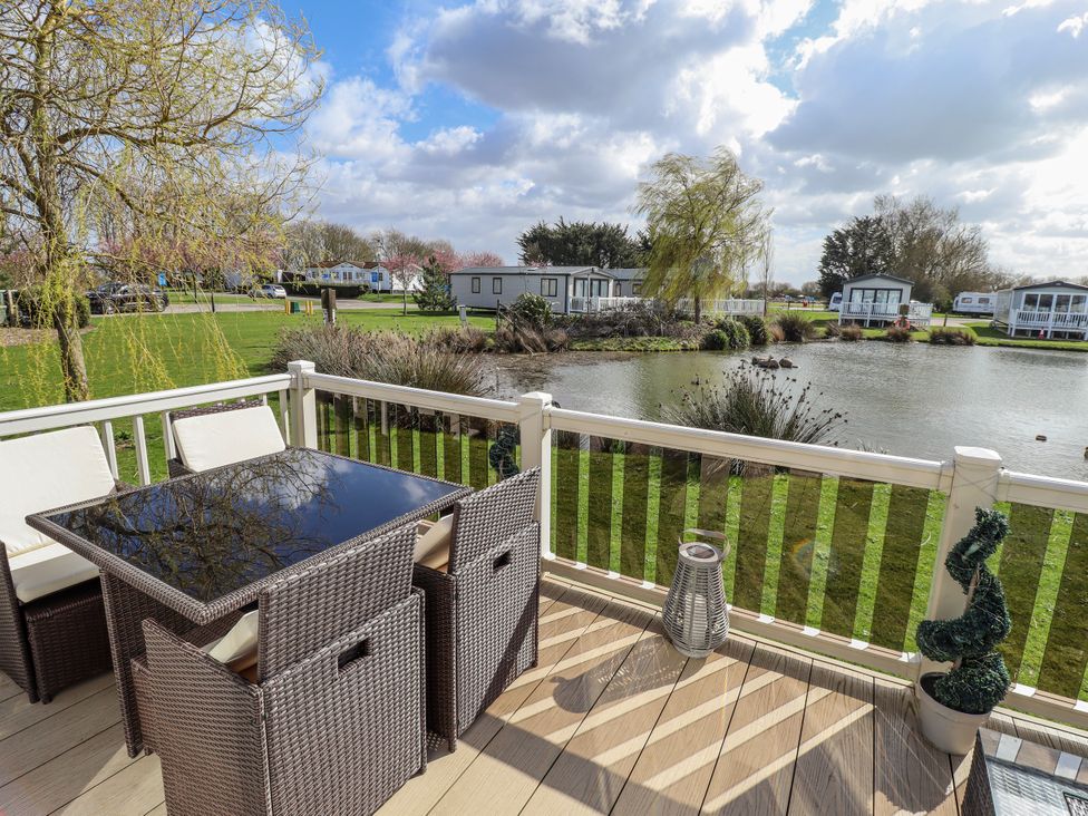 An outdoor seating area with a table and chairs overlooking a pond at 13 The Lakes in Mablethorpe