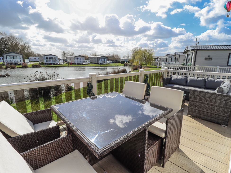 An outdoor area with a table and chairs near a lake at 13 The Lakes Mablethorpe
