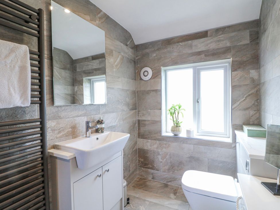 A bathroom with a sink, toilet, mirror, and window at Brecks Cottage in Moorhouse near Tuxford