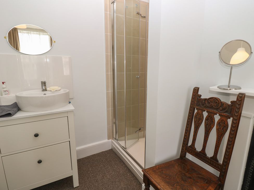 A bathroom with a shower, sink, and a wooden chair at Bay Tree Cottage in Shanklin