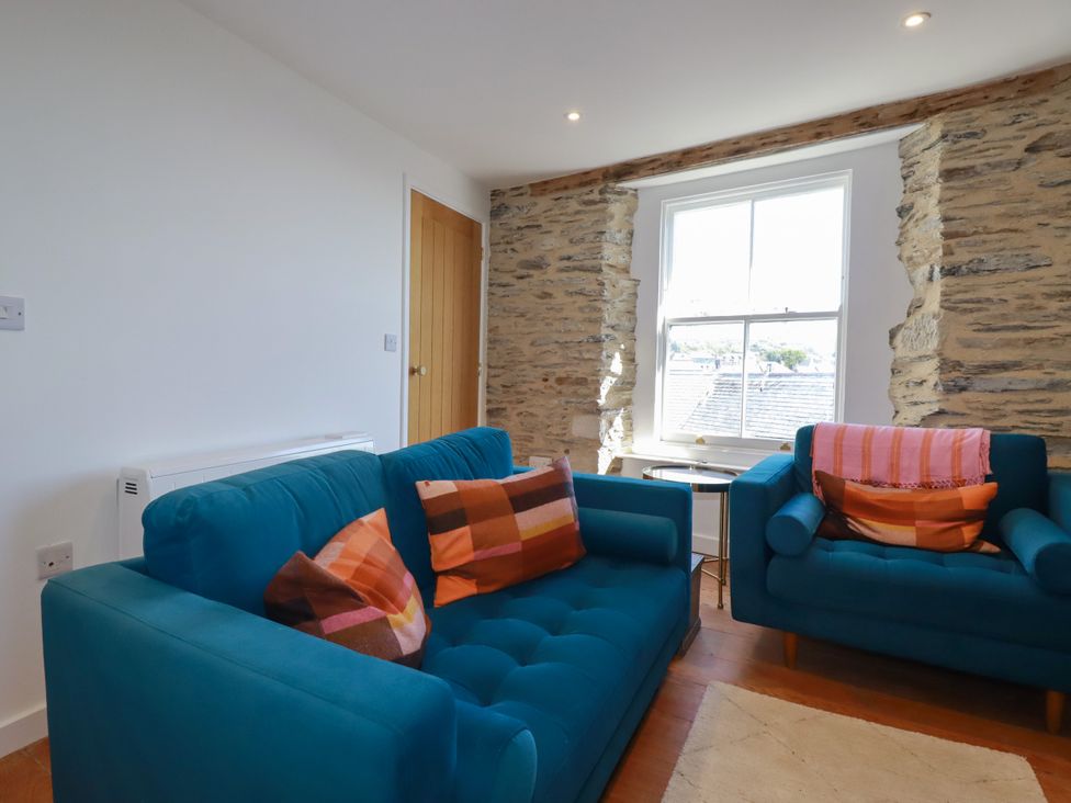 A living room with a sofa, armchair, and window at Whalebone Cottage in St. Austell