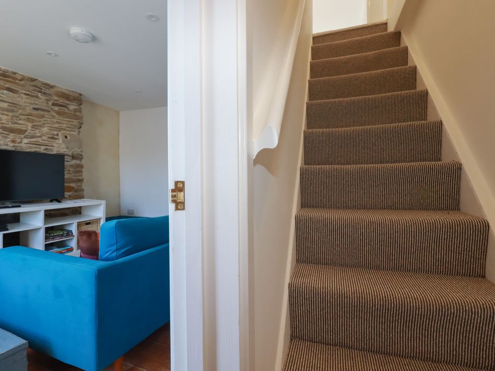 A view of stairs leading from a living room with a television and sofa at Whalebone Cottage in St. Austell