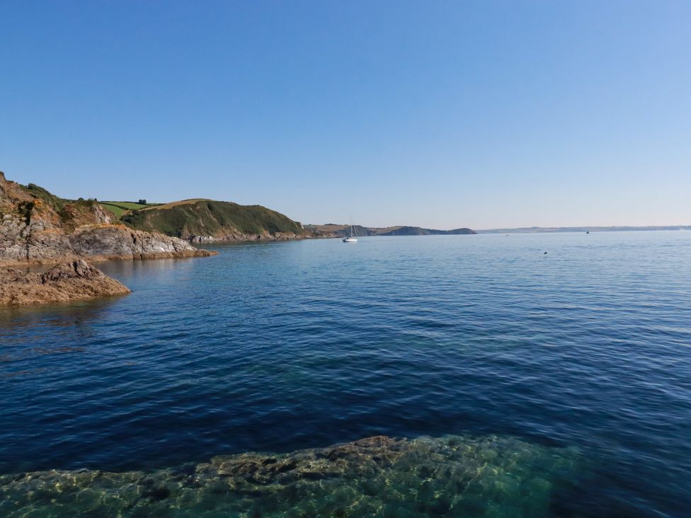 A view of water and hills with a boat in the distance at Whalebone Cottage in St. Austell