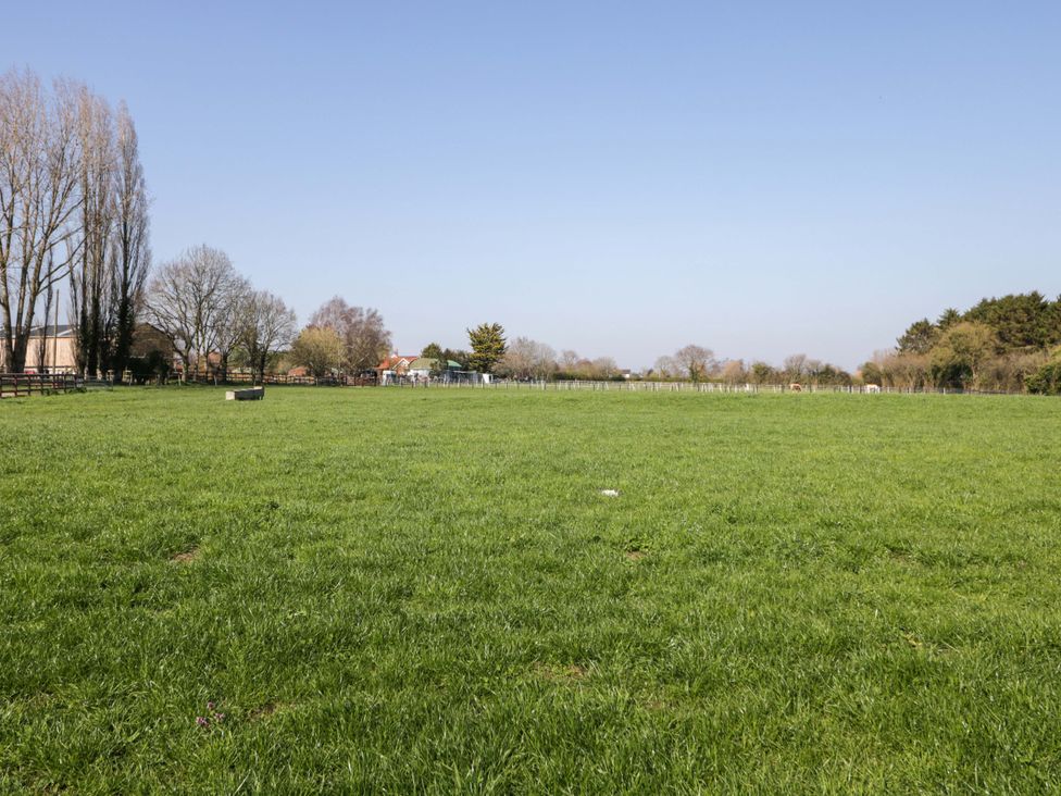 A grassy field with trees and houses in the background at 3 Woods Farm House in Chippenham