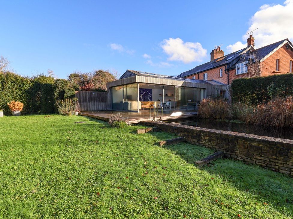 A garden with a modern house and pond at Bredy Cottages in Burton Bradstock