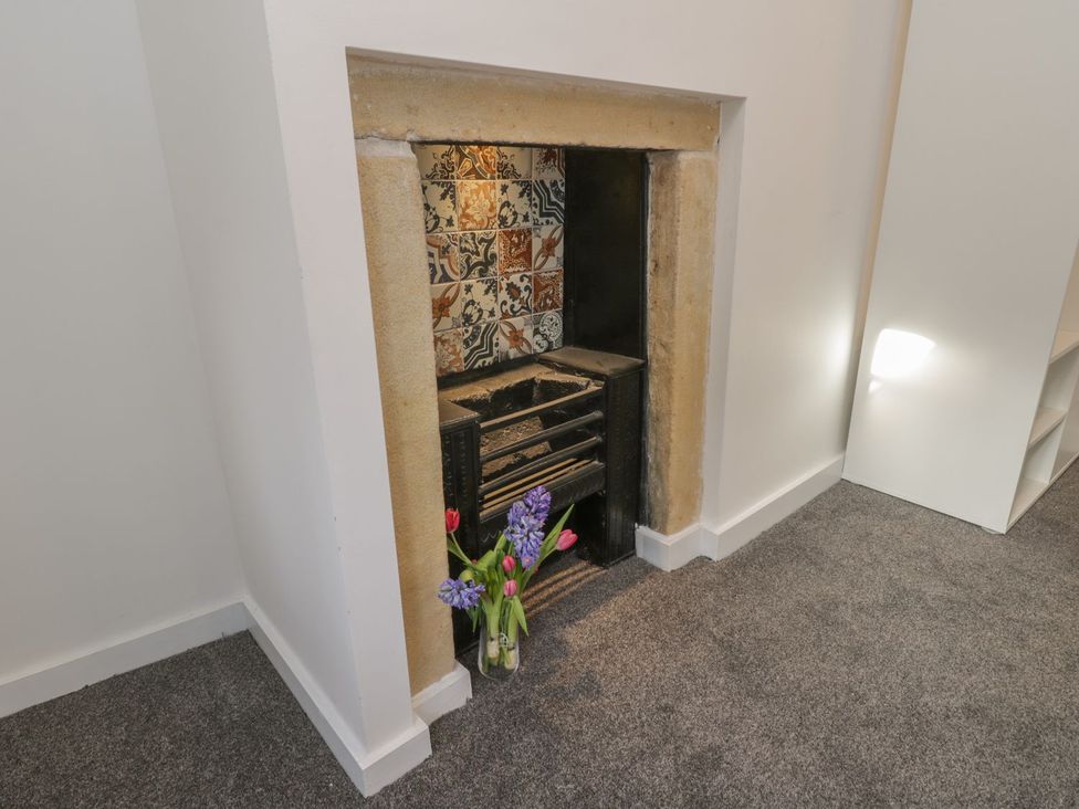 A fireplace with decorative tiles and flowers in a vase at 47A Baxtergate in Whitby