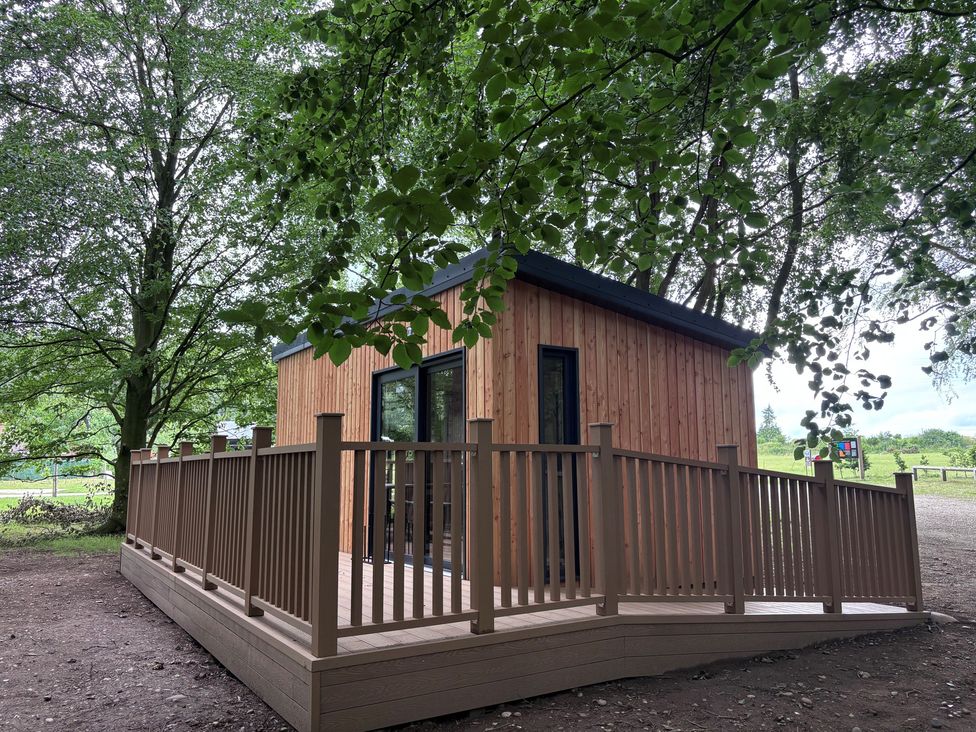 A wooden cabin with a decking area surrounded by trees at Sherwood Pines - Deluxe Pod 1 near Edwinstowe